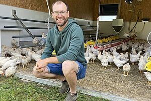 Un homme à genoux devant son troupeau de poules.