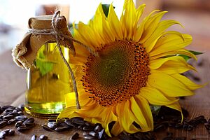 Une bouteille d'huile de tournesol est posée devant un tournesol et des graines de tournesol sur une table.