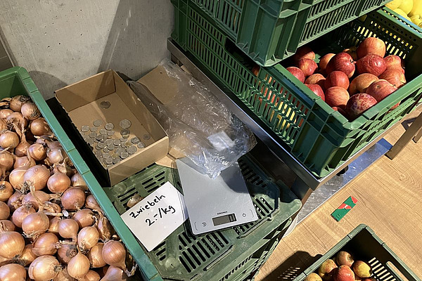 Stand de vente ouvert avec des oignons, des pommes, une balance et une caisse avec des pièces de monnaie.